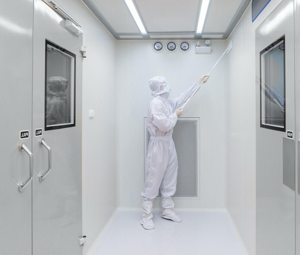 The inside of a sterile white room, with an employee dressed in white PPE cleaning one of the walls